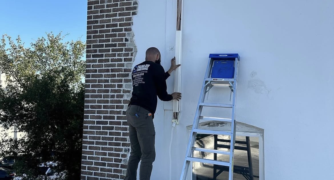 Technician installing line set on exterior wall